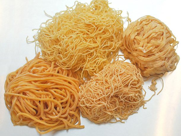 Overhead view of four types of fresh Chinese egg noodles, arranged in small piles.