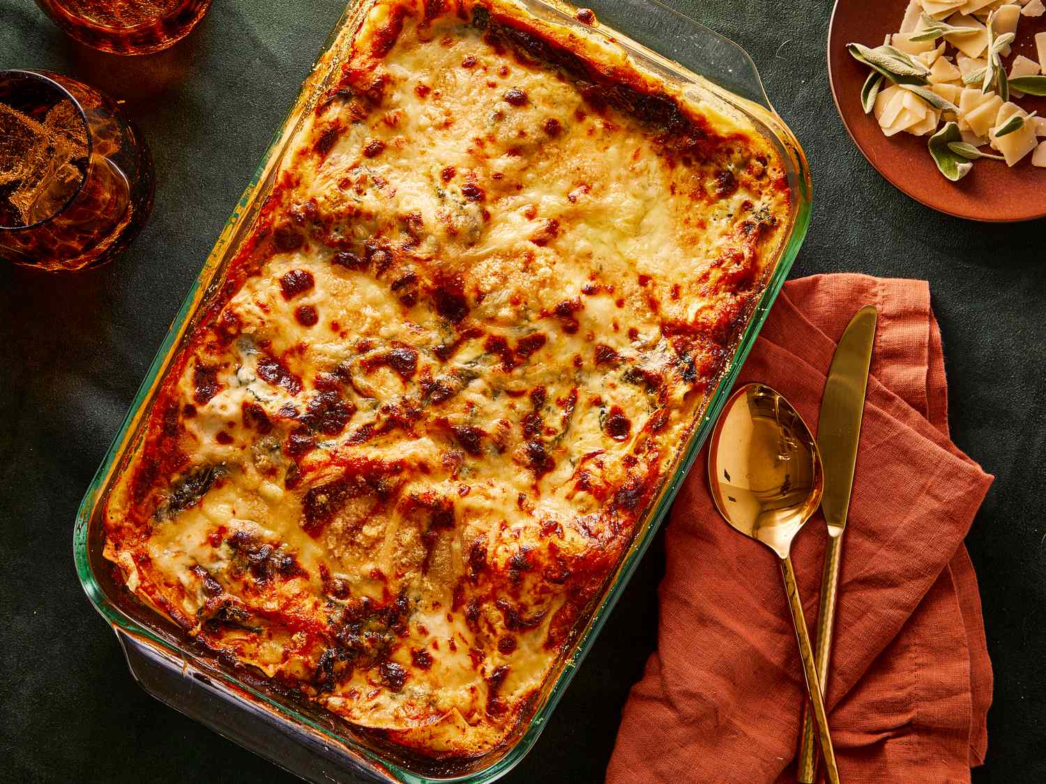 A baked lasagna in a glass dish with utensils and a napkin on the side