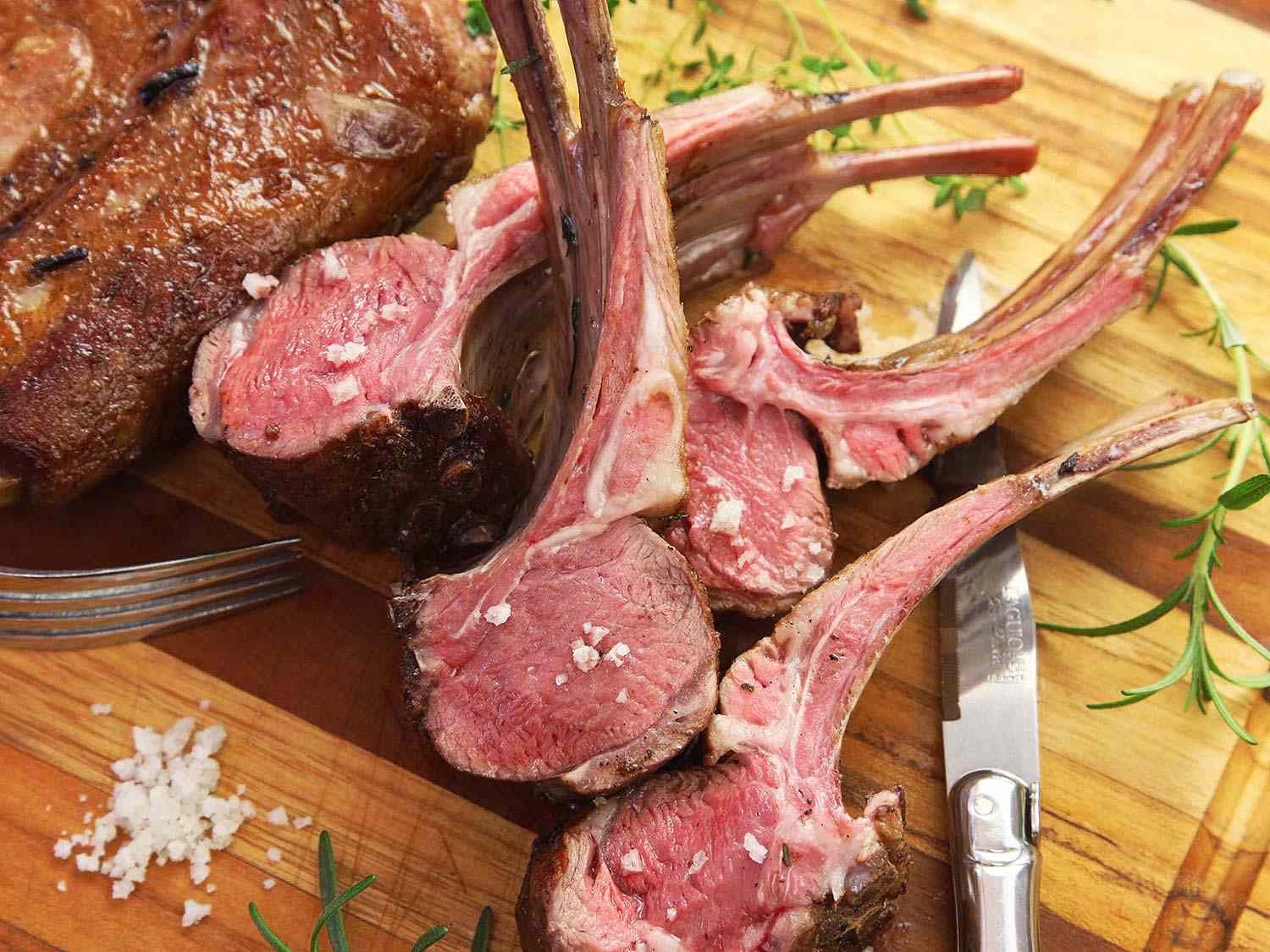 Some sliced rare lamb chops from a sous vide rack of lamb on a wooden cutting board. 