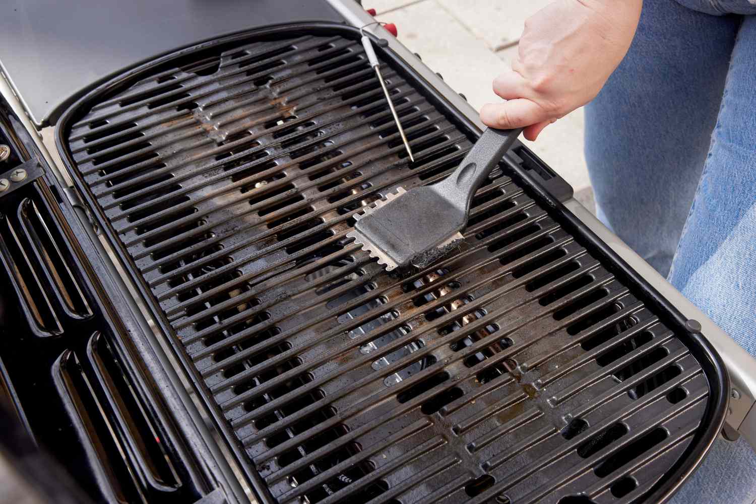 A person using a grill brush to clean the grates of a portable gas grill.