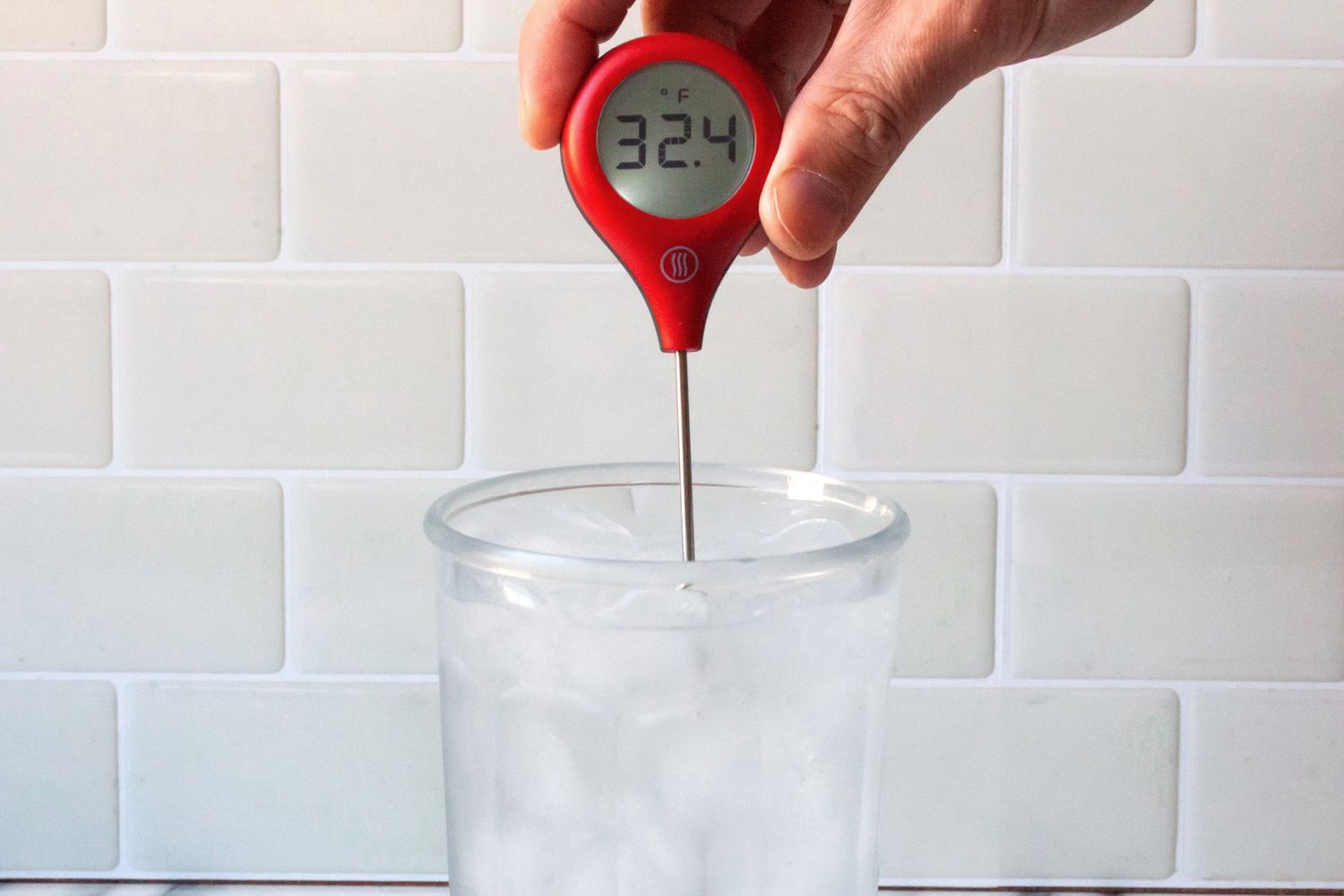 A person using a red ThermoWorks Thermopop to take the temperature of ice water.