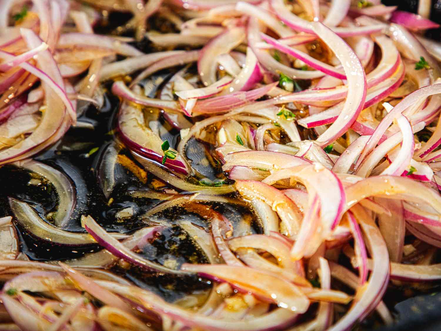 Thinly sliced onions cooking in a pan with oil and herbs