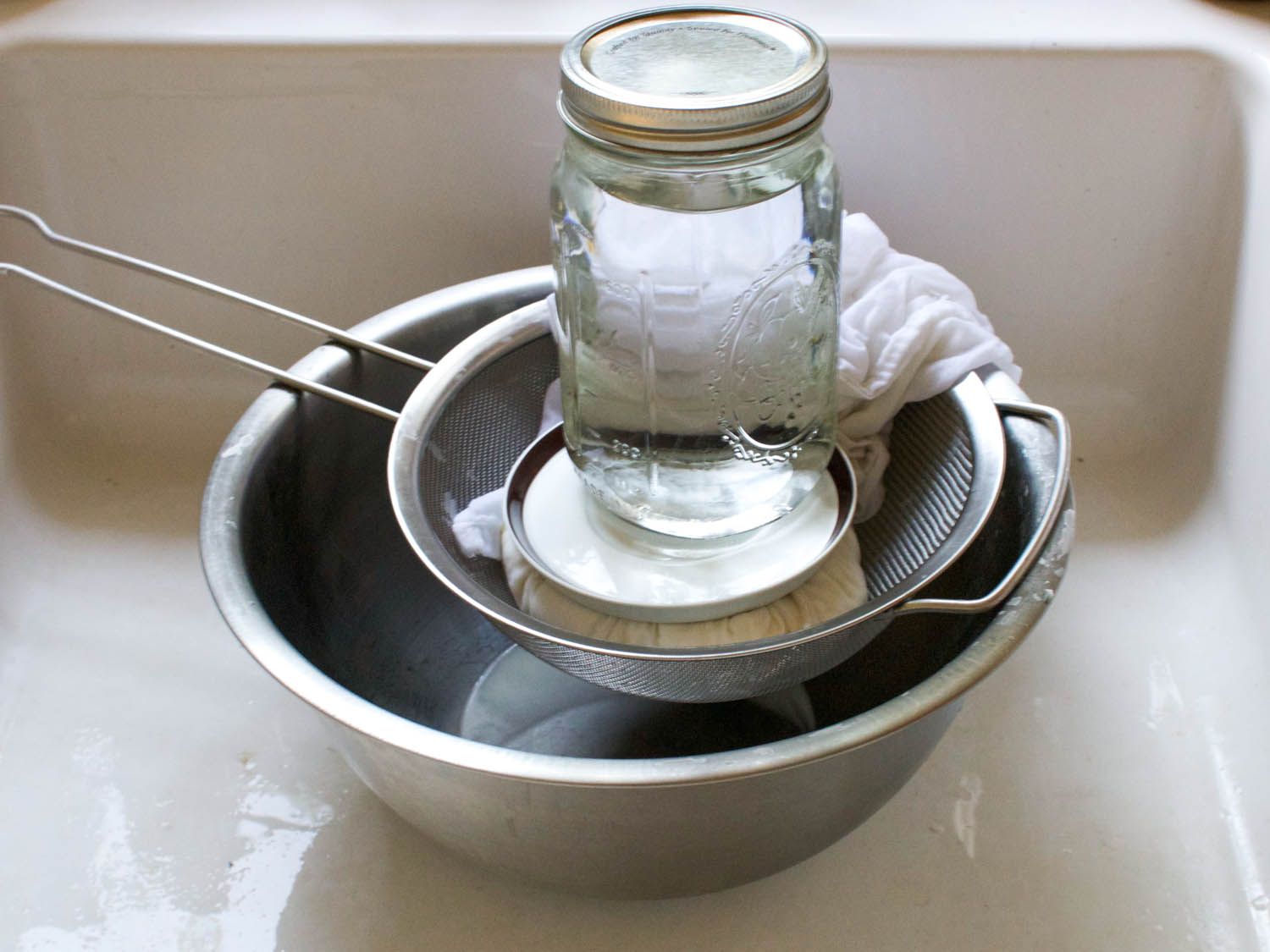 Using a water-filled mason jar as a weight for pressing curds in a colander to drain it fully.