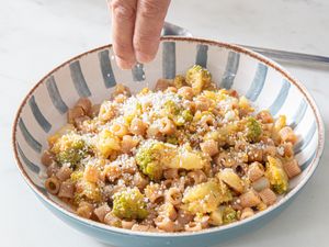 A bowl of pasta with Romanesco broccoli being sprinkled with grated cheese by a hand