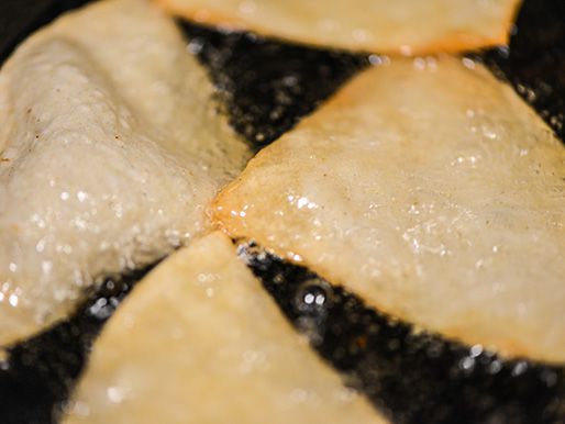 Quartered corn tortillas being shallow-fried in a skillet.