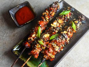 Overhead view of Crispy Caramelized Chicken Skewers, served on a dark green rectangular platter.