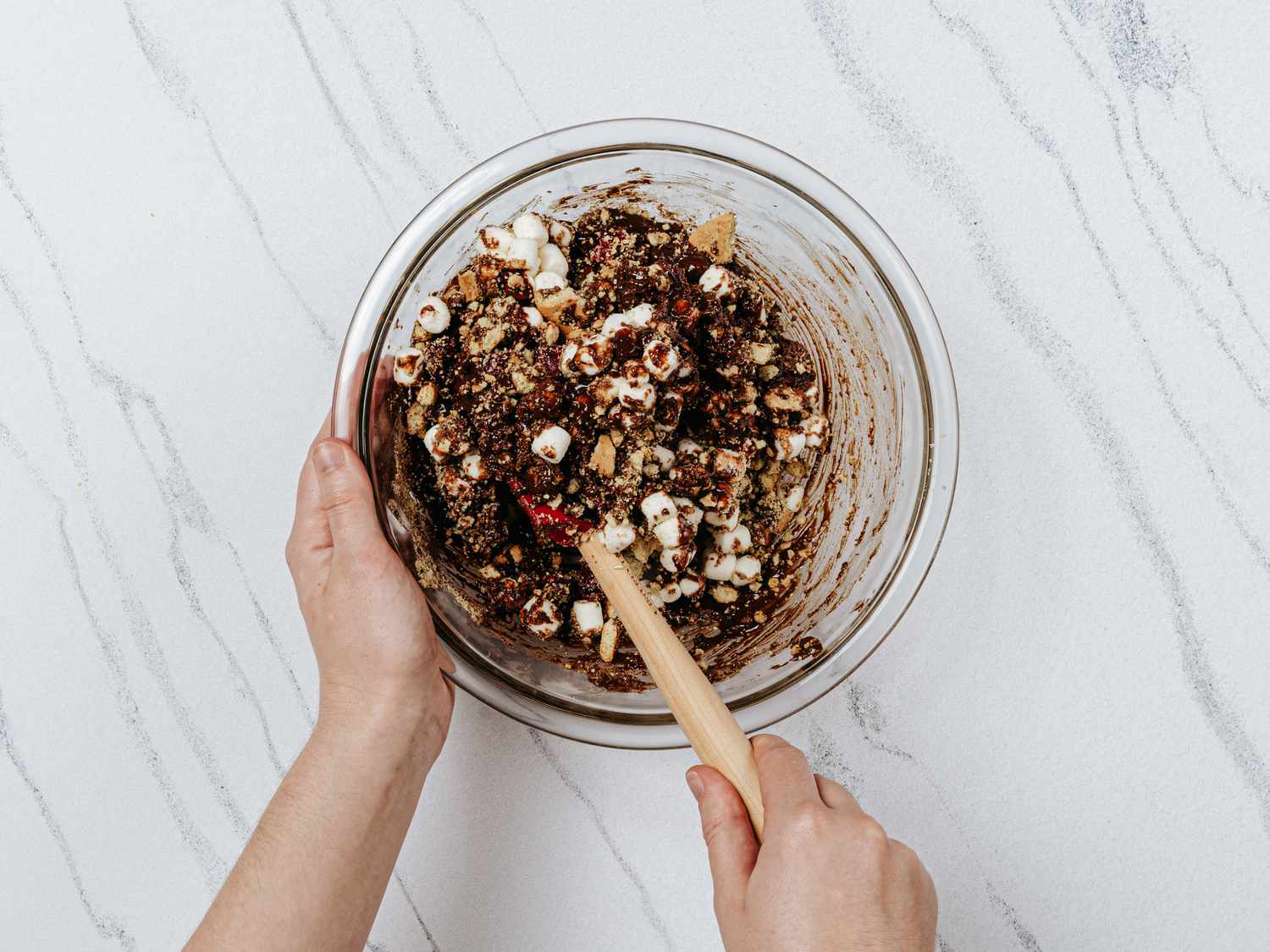Adding digestive biscuits, marshmallows and cherries into chocolate mixture in a bowl