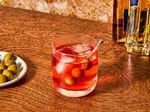 Glass of cocktail with ice and olives on side plate