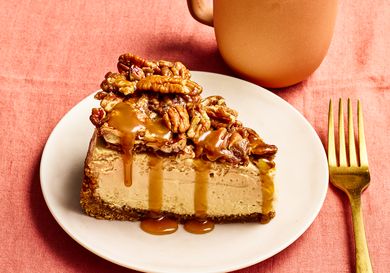 Slice of pecan pie cheesecake on a plate with a fork and mug on a table