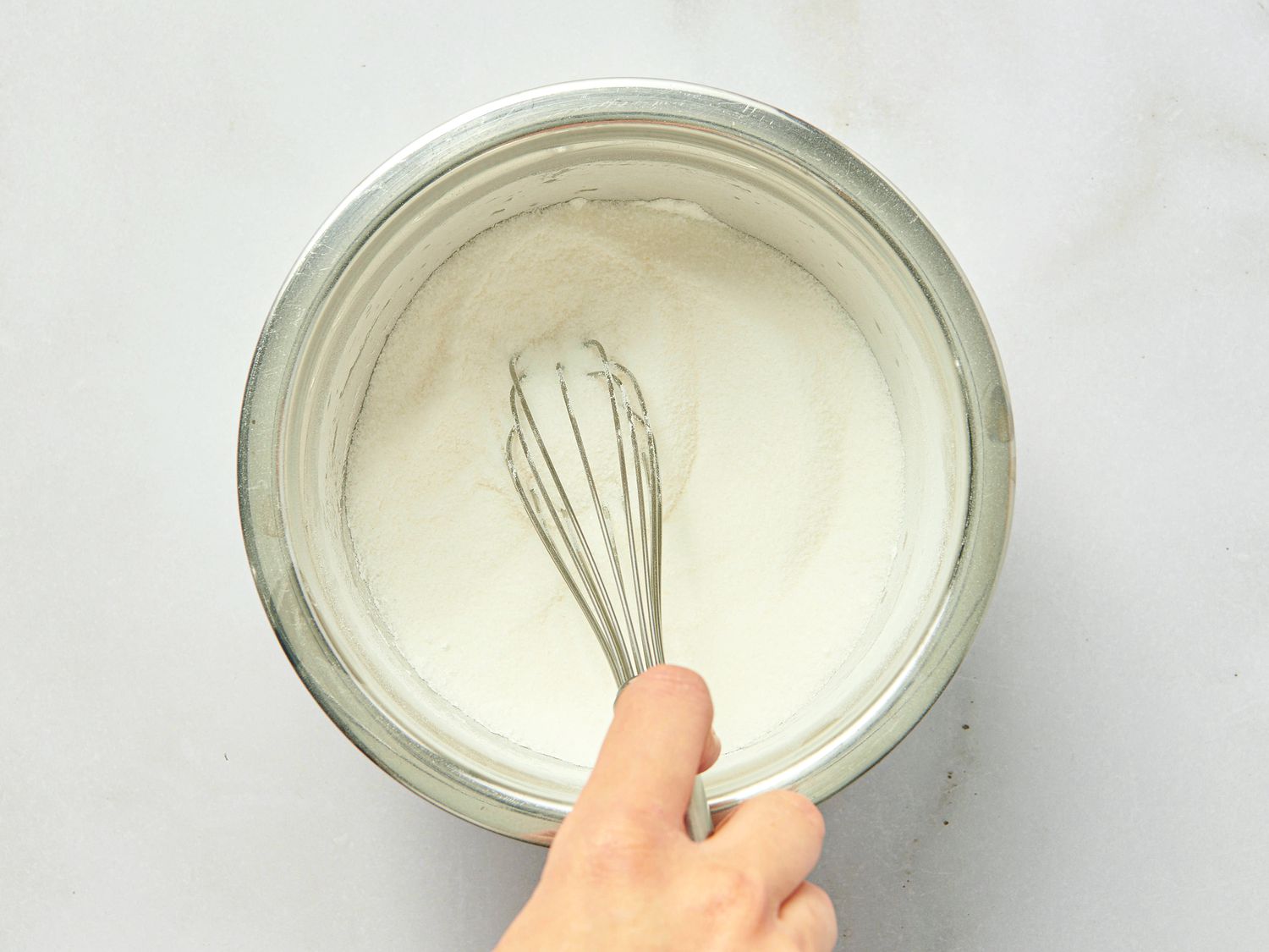 A hand whisking a white mixture in a metallic bowl