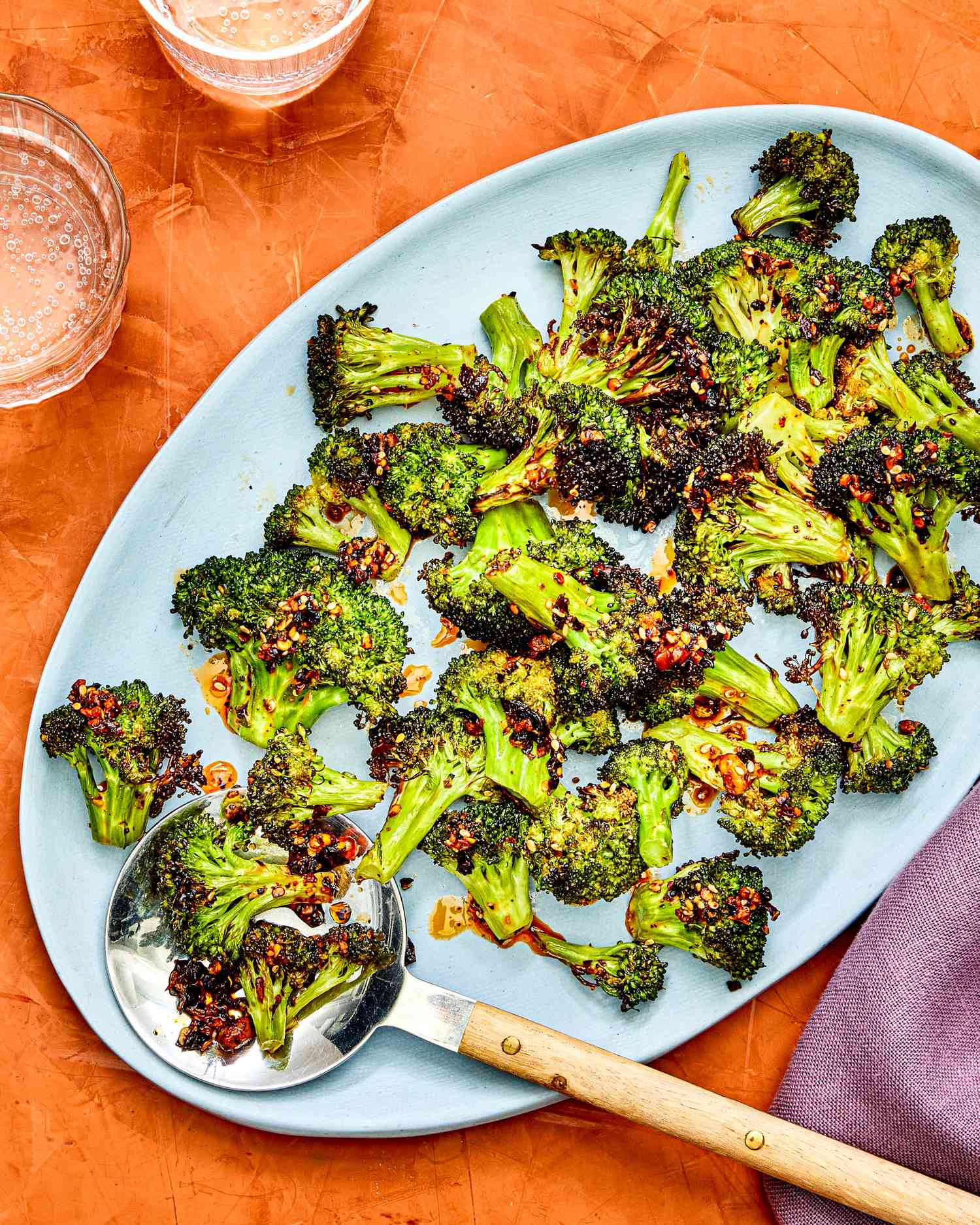 Air-fried broccoli on a blue platter against an orange background.