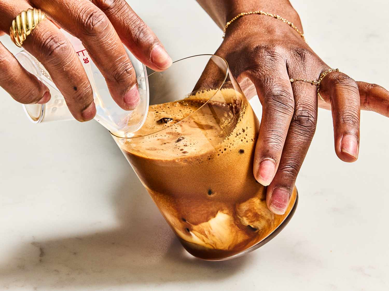 Pouring prepared coffee into a glass with ice close up of hands holding a pitcher and the glass