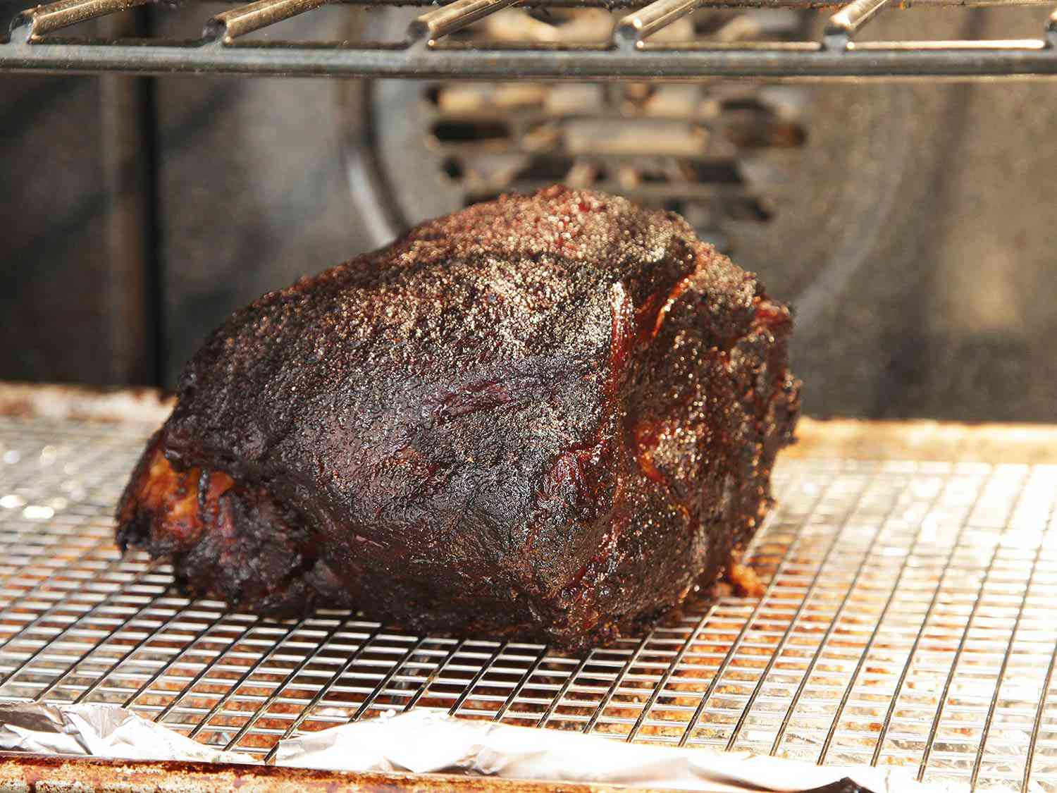 Pork shoulder on a baking rack in an oven being cooked to develop a crust 