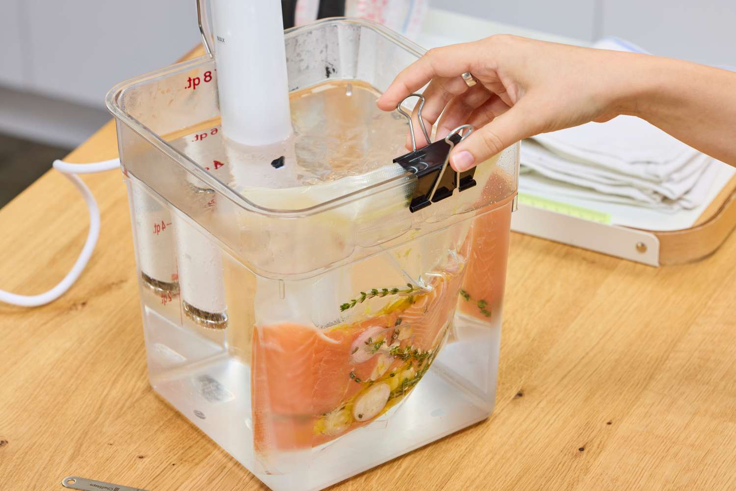 Breville Joule Turbo Sous Vide Machine setup with a hand holding a bag containing food and herbs immersed in water