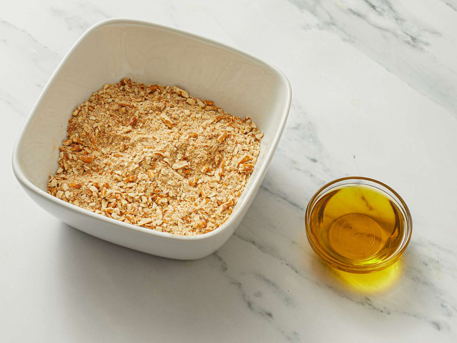 Bread crumbs in a square bowl, small bowl of olive oil next to it.