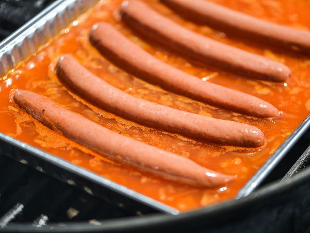 Natural casing hotdogs floating in the aluminum pan filled with poaching liquid.