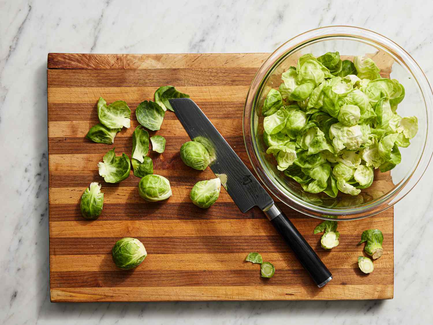 Overhead view of brussels sprouts leaves being separated on a cutting board 