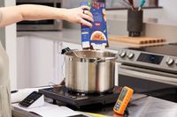 A person pouring pasta from a box into a pot on a stovetop in a kitchen