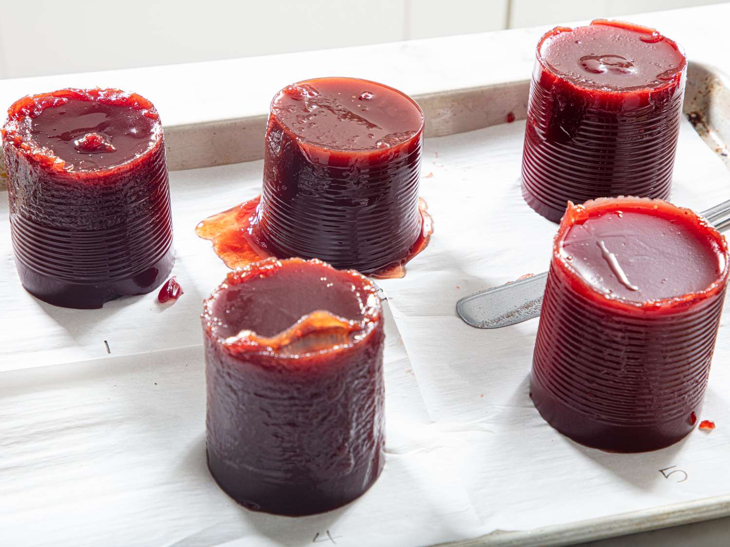 Cylindrical servings of cranberry sauce placed on a metal tray lined with parchment paper
