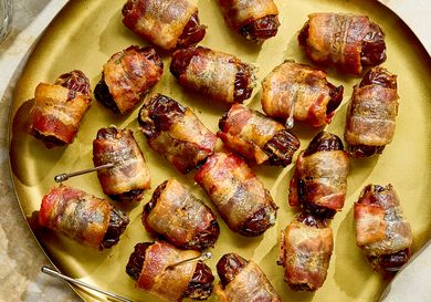 A plate of baconwrapped appetizers on a countertop served with small dishes and drink glasses