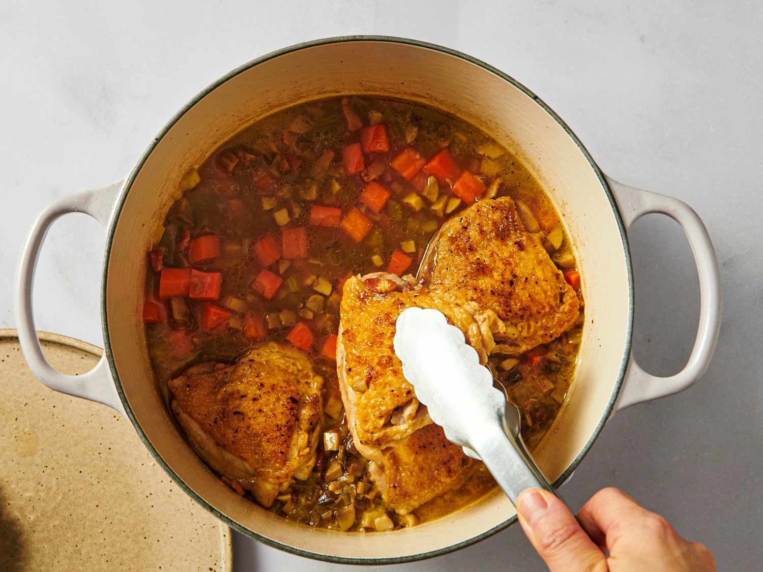 Chicken and vegetables cooking in a pot a hand using tongs to adjust the food