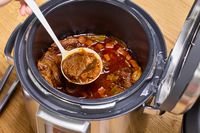 A person spoons cooked meat and vegetables from the Breville the Fast Slow Pro