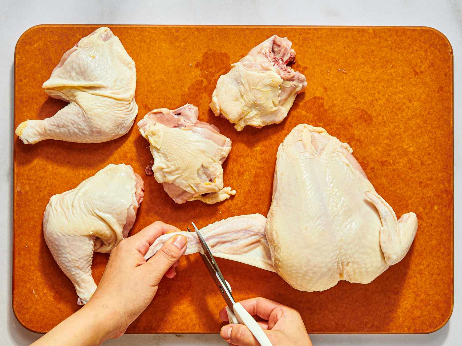 Chicken being cut up, while hands trim some fat off the wings off