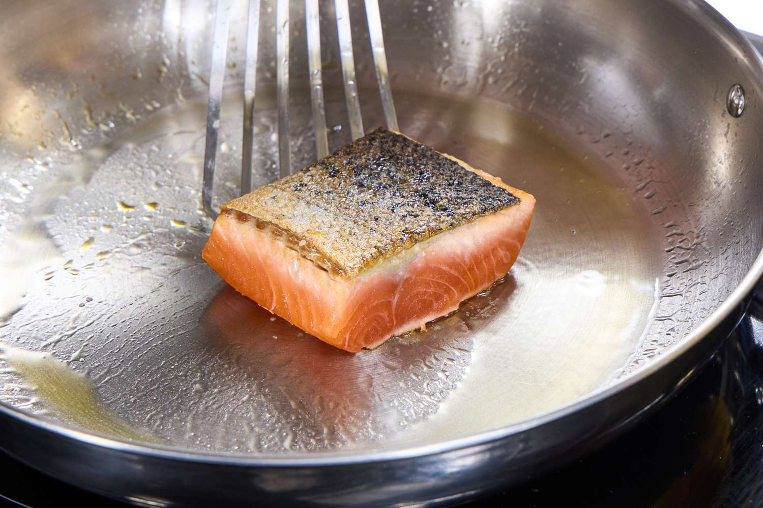 A person cooks a piece of salmon in the Tramontina 12-Inch Stainless Steel Skillet