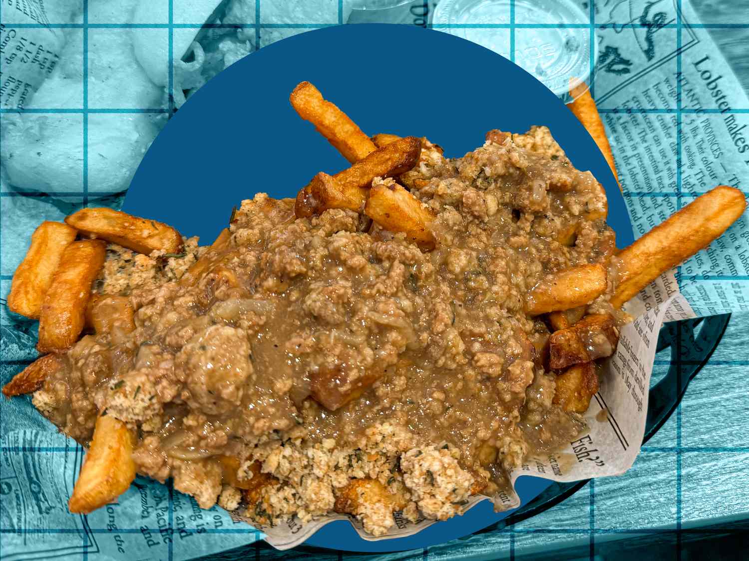 A plate of fries topped with minced meat and a sauce on a background resembling a blue grid and newspaper