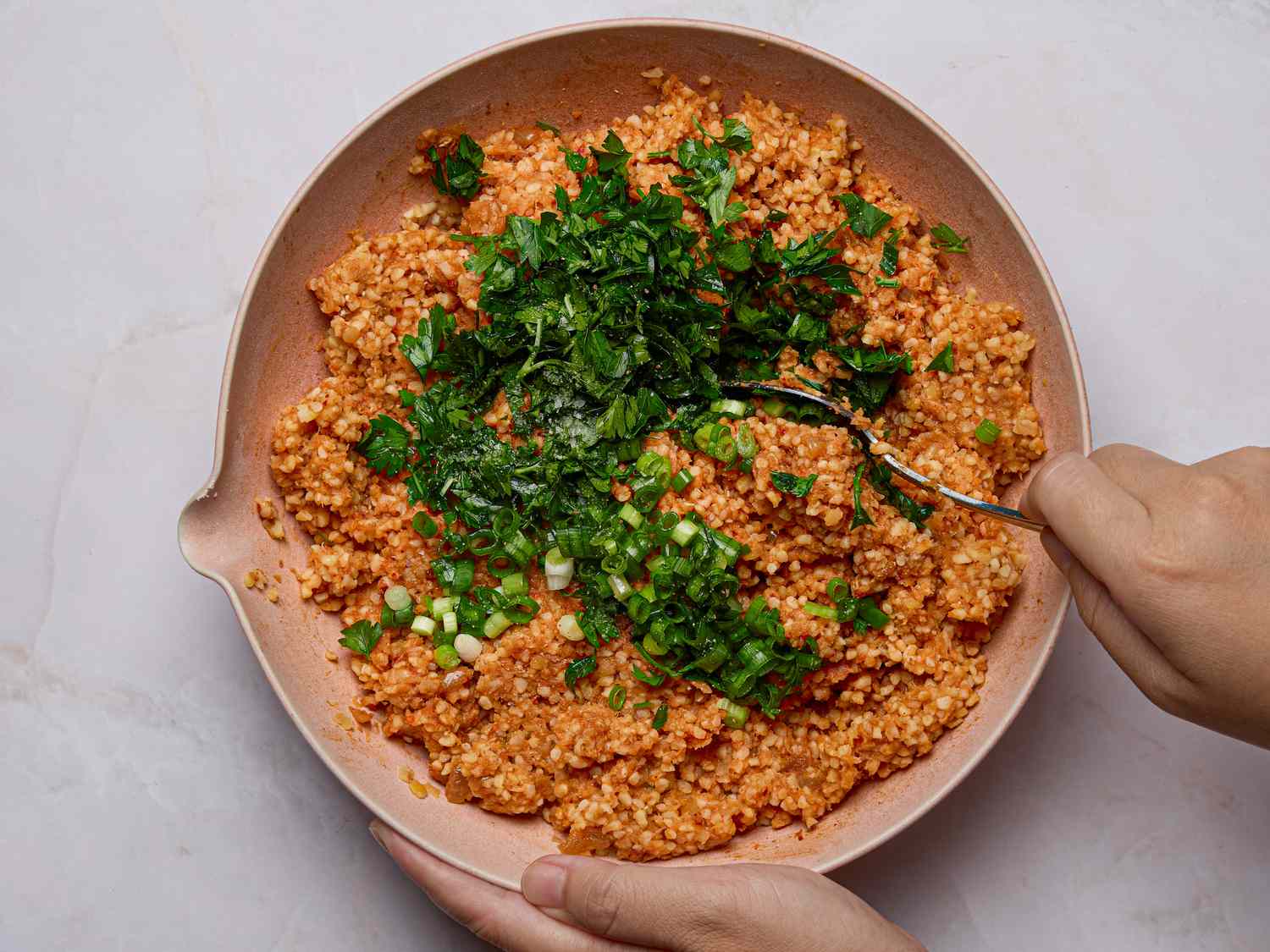 Hands mixing lentil and herb mixture in a shallow bowl with a fork