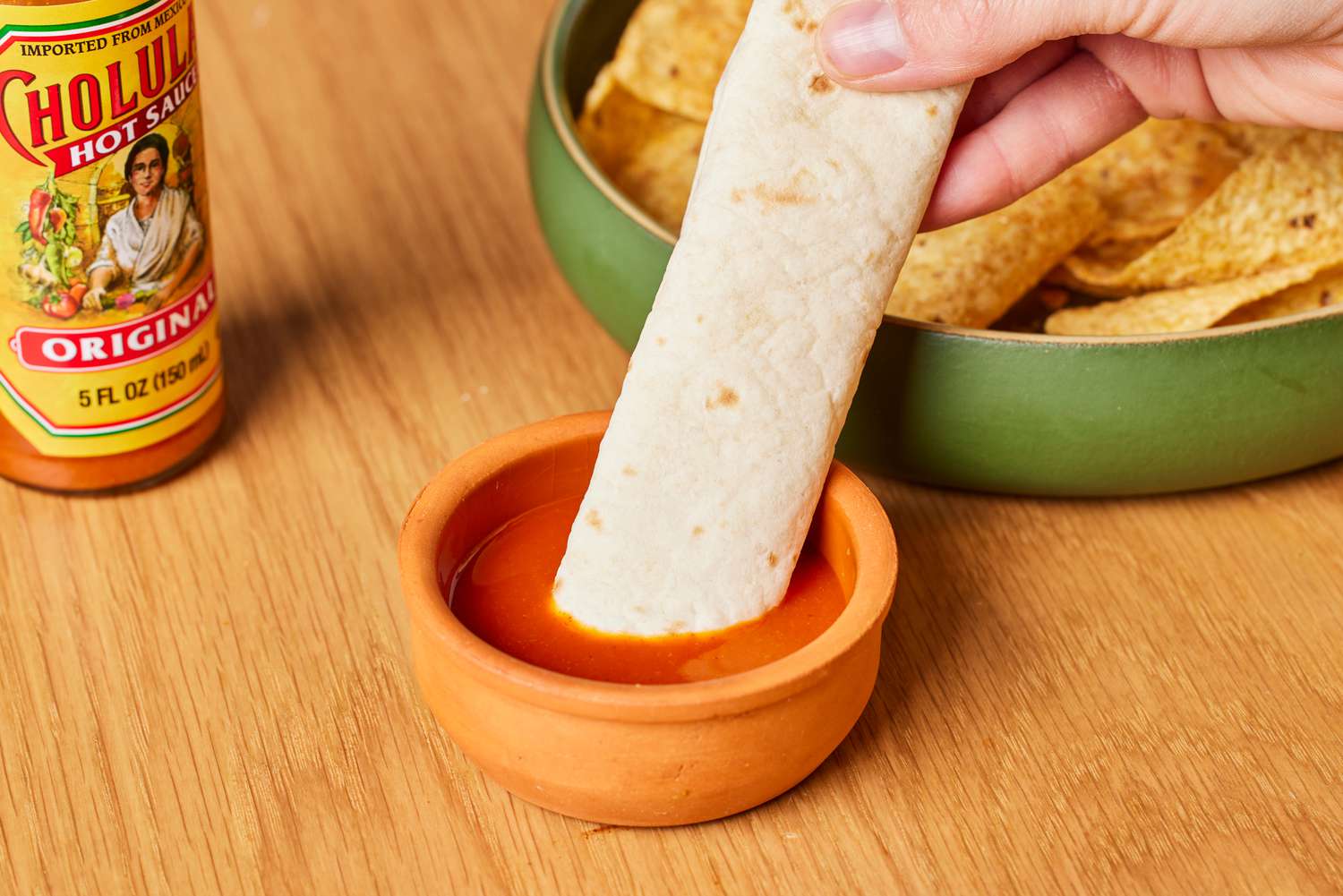 person dipping tortilla in Cholula Original Hot Sauce