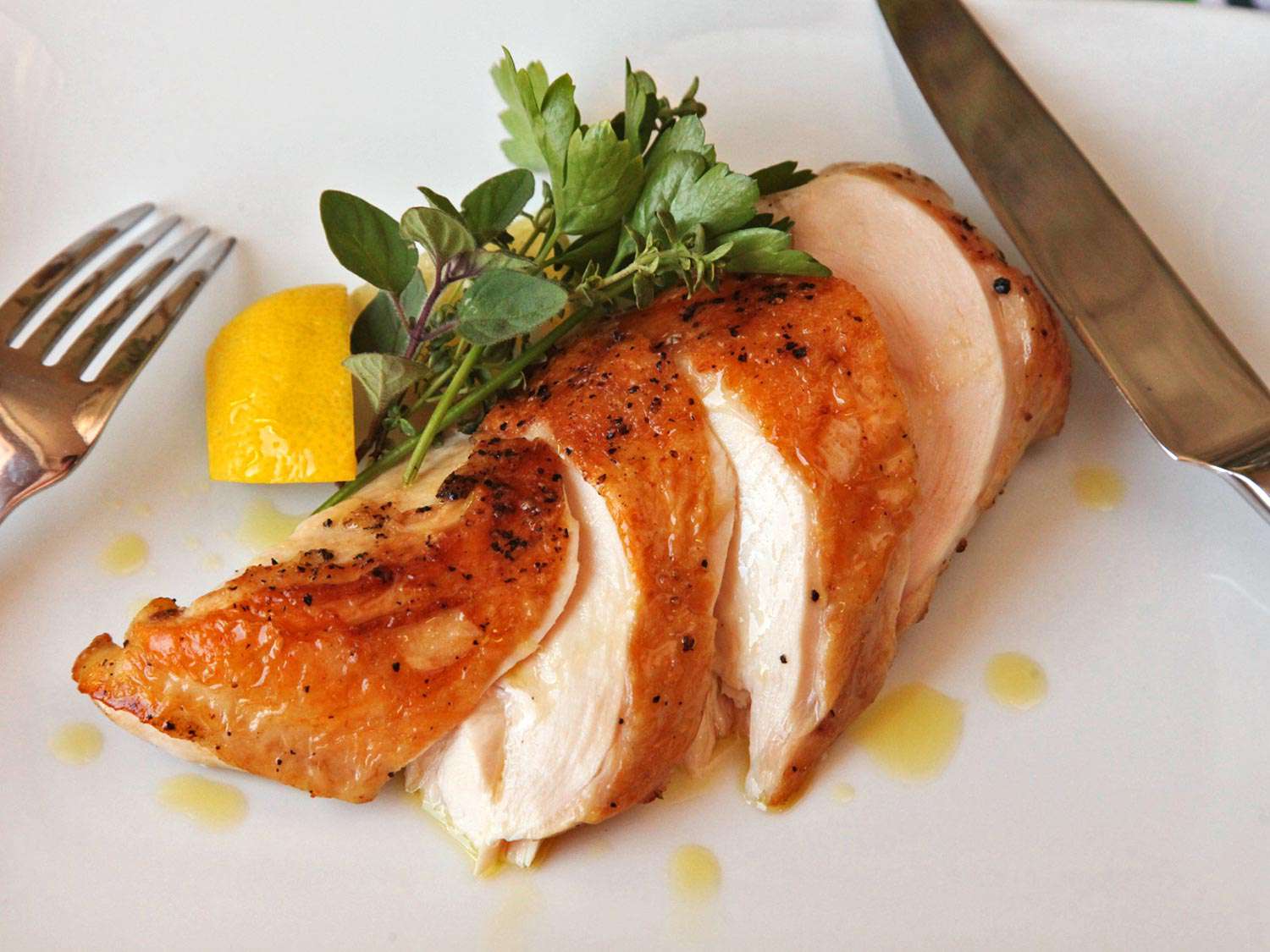 Sliced sous vide chicken breast on a plate, garnished with herbs and lemon.