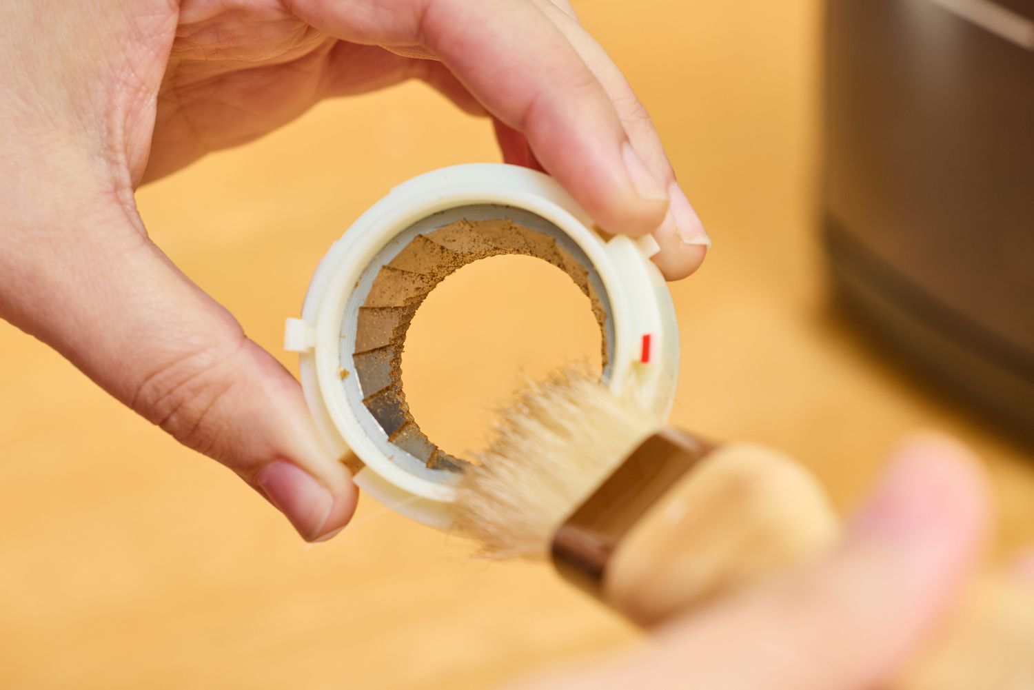 A person brushes a part from the Baratza Encore Conical Burr Coffee Grinder