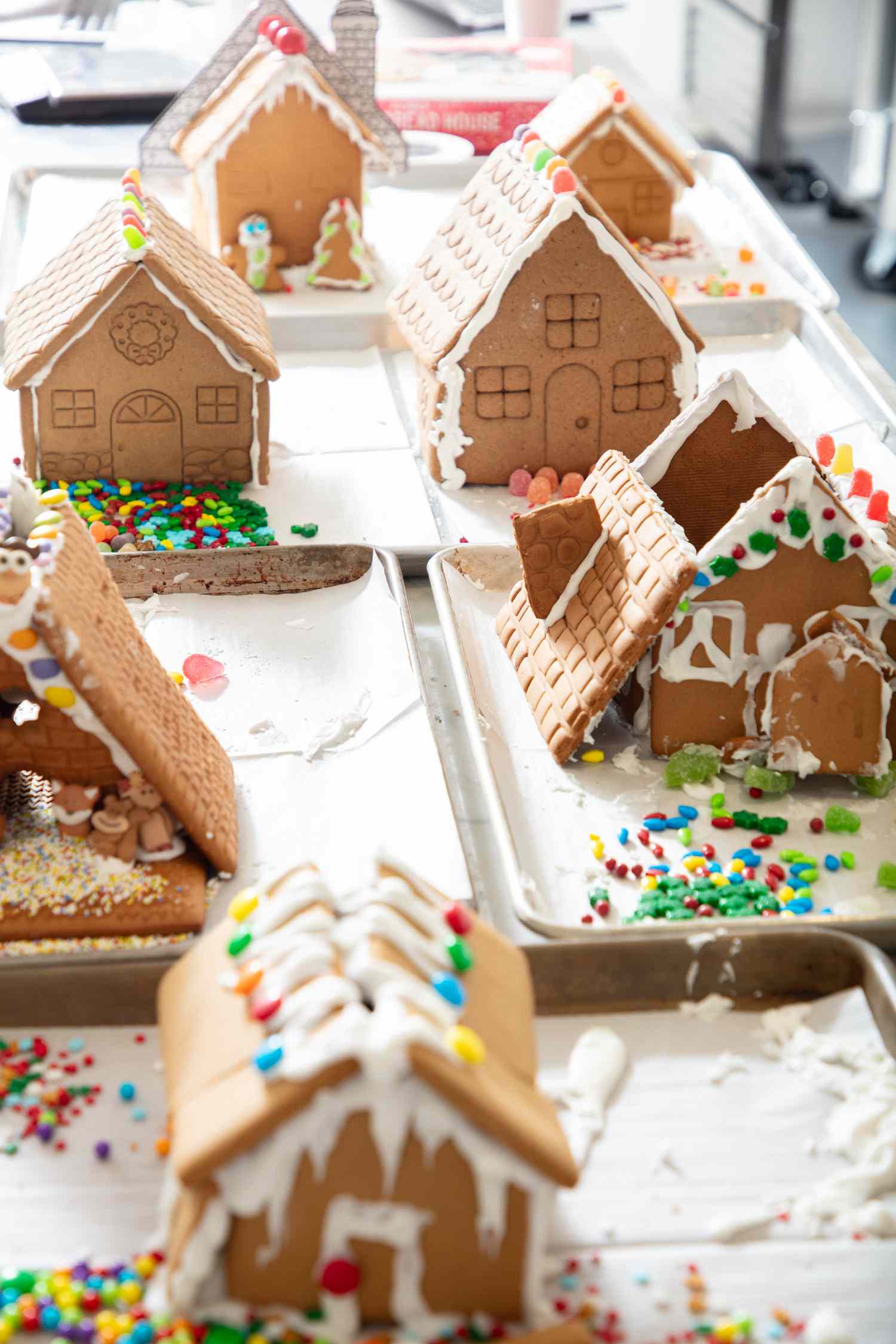 A variety of decorated gingerbread houses on trays some with candy and icing details