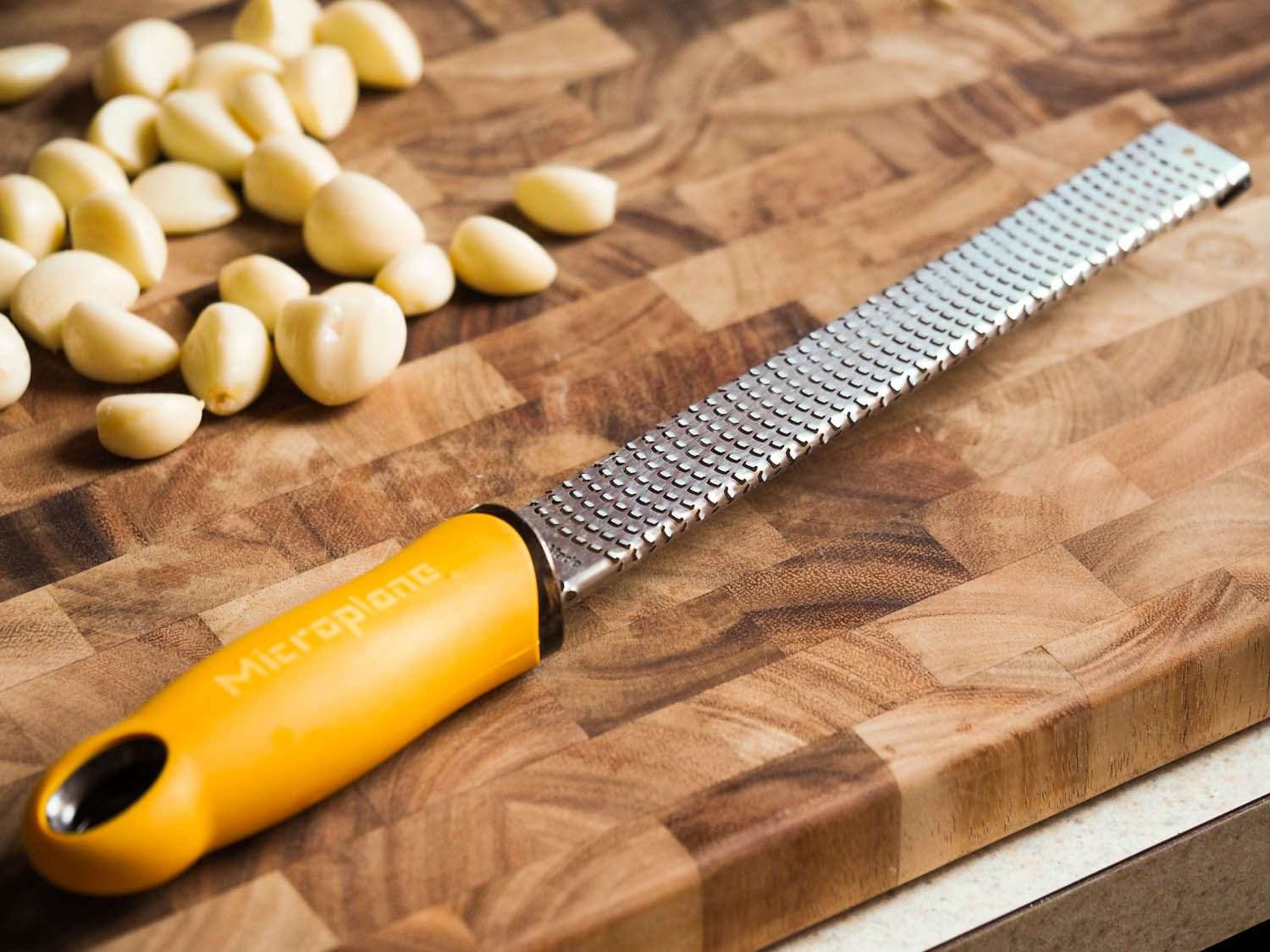 A Microplane grater on a cutting board next to whole garlic cloves.
