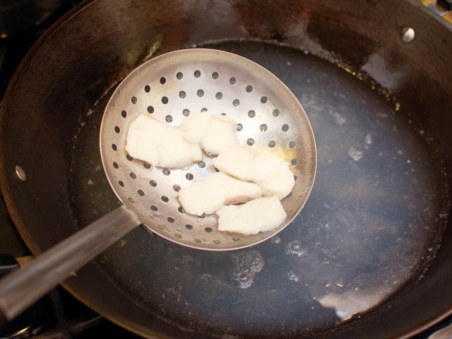 Cooked chicken being pulled out of a wok with a slotted spoon.