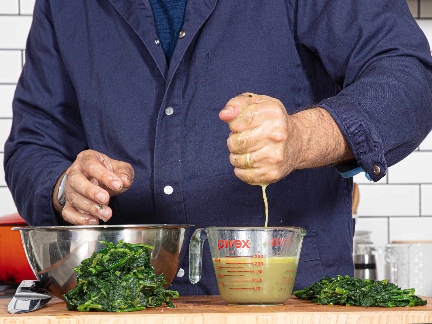 A person squeezing water out of spinach into a measuring cup on a kitchen counter