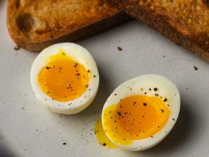 A perfect soft-boiled egg, cut in half to reveal the runny yolk, with toasted bread at the top of the image.