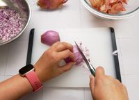 a person mincing a shallot with a paring knife
