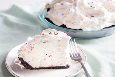 A slice of no-churn vanilla ice cream pie, served on a white speckled dish. The rest of the pie is nearby.