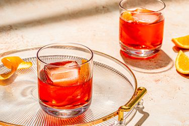 Two Negroni cocktails served in old-fashioned glasses with orange peels, with one served on a glass tray