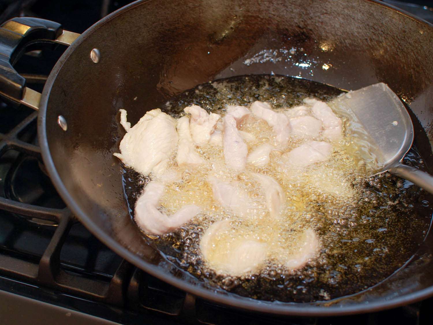 Chicken being oil-blanched in a wok.