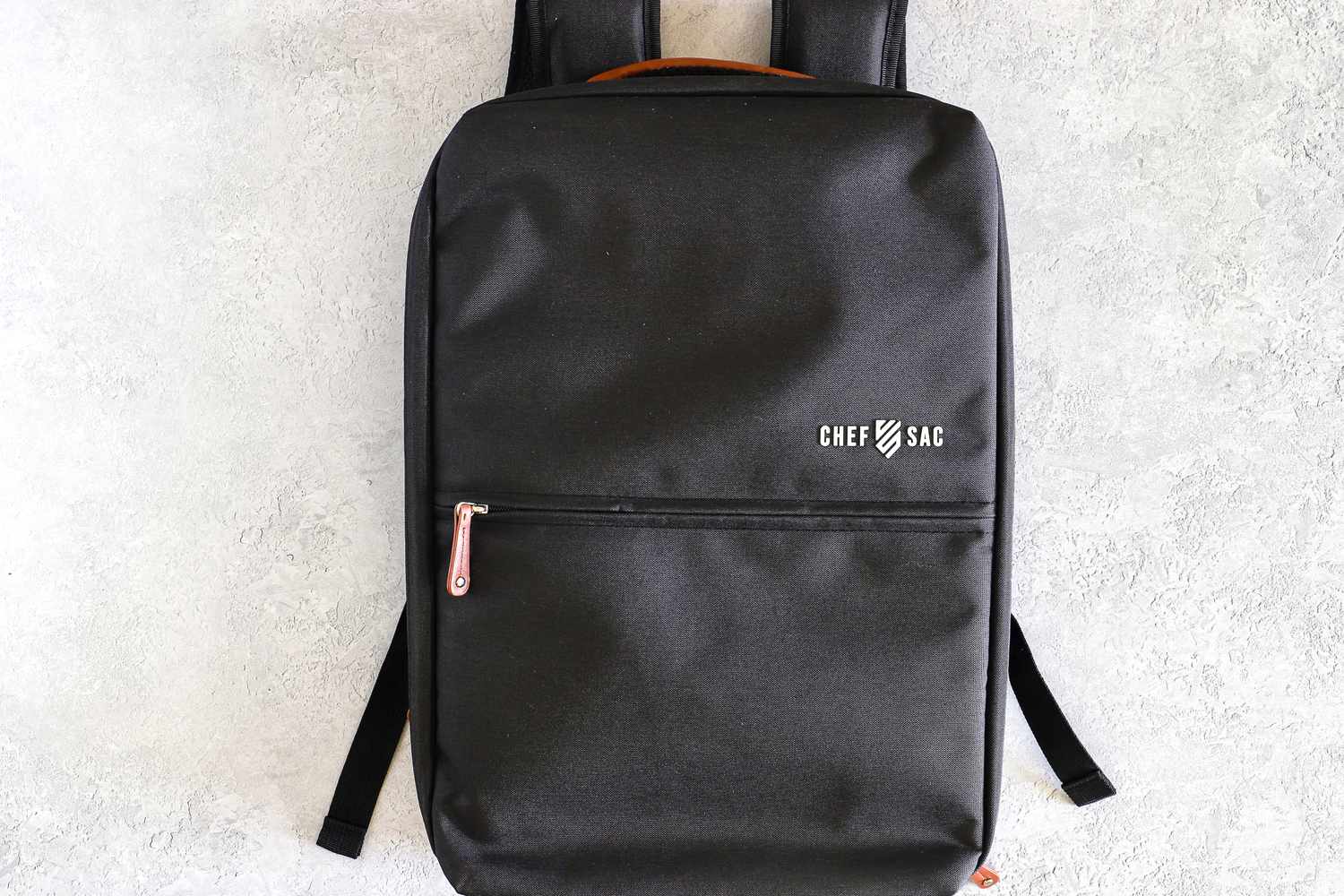 A Chef Sac backpack displayed on a light surface featuring a clean and minimalist design with a logo and front pocket