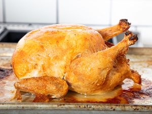 A roasted chicken placed on a baking tray photographed in a kitchen setting