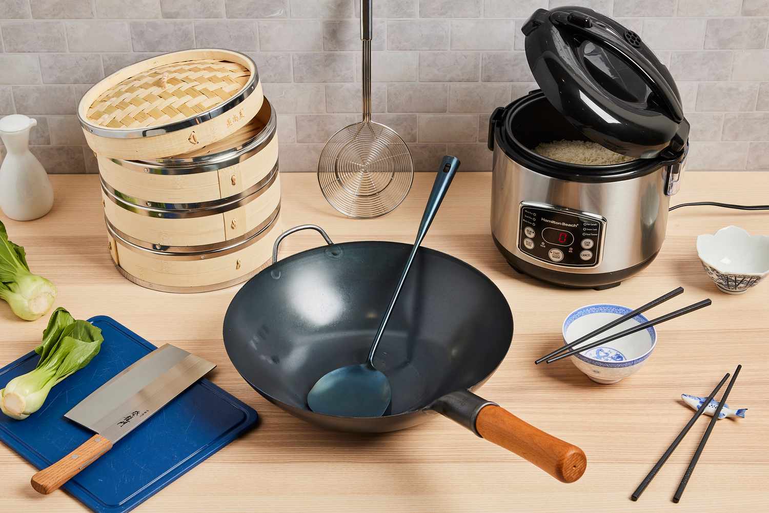 a wooden countertop with a rice cooker, wok chuan, wok, cleaver, and more. 