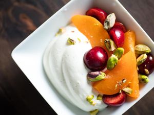 Overhead shot of a bowl of summer fruits and whipped Greek yogurt garnished with pistachios.