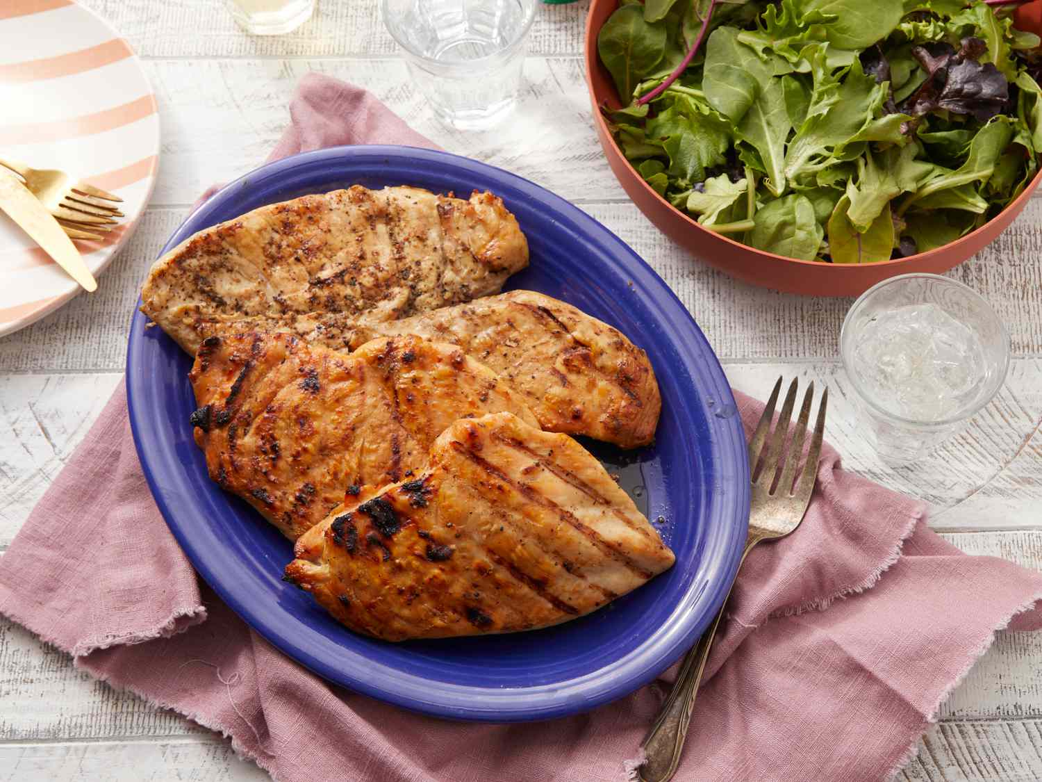 Grilled chicken breasts on a blue plate with salad nearby