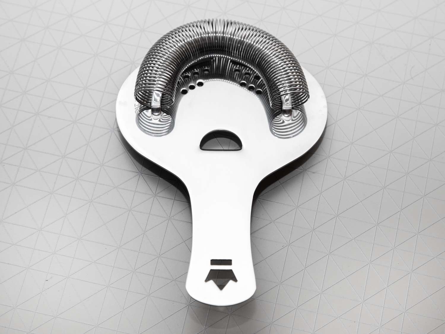 A stainless steel hawthorne strainer set on a grey surface