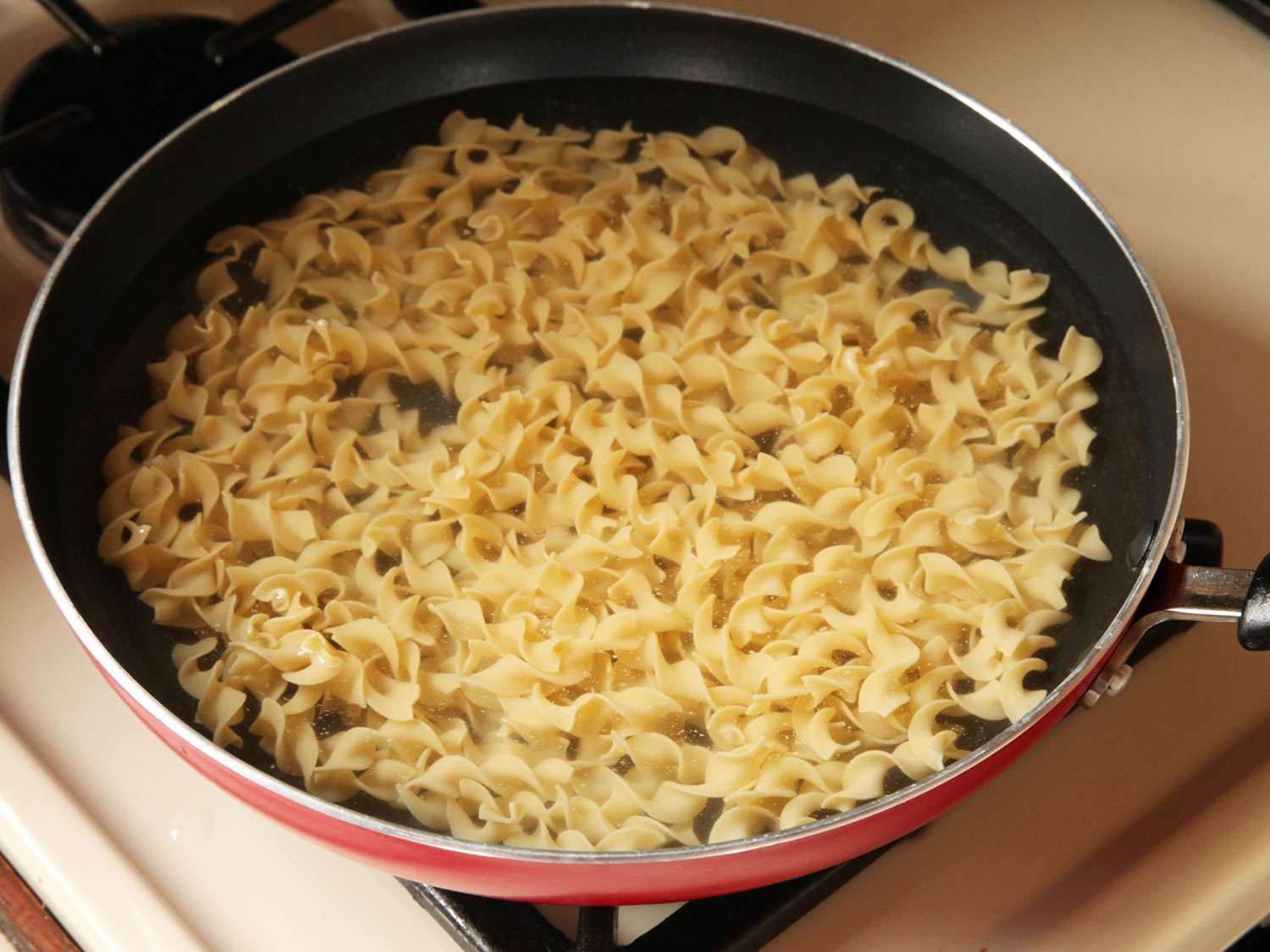 Pasta submerged in water in a skillet.