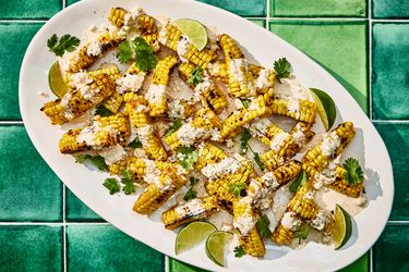 Bright colorful photo of grilled corn, topped with sauce, cheese cilantro and limes. 